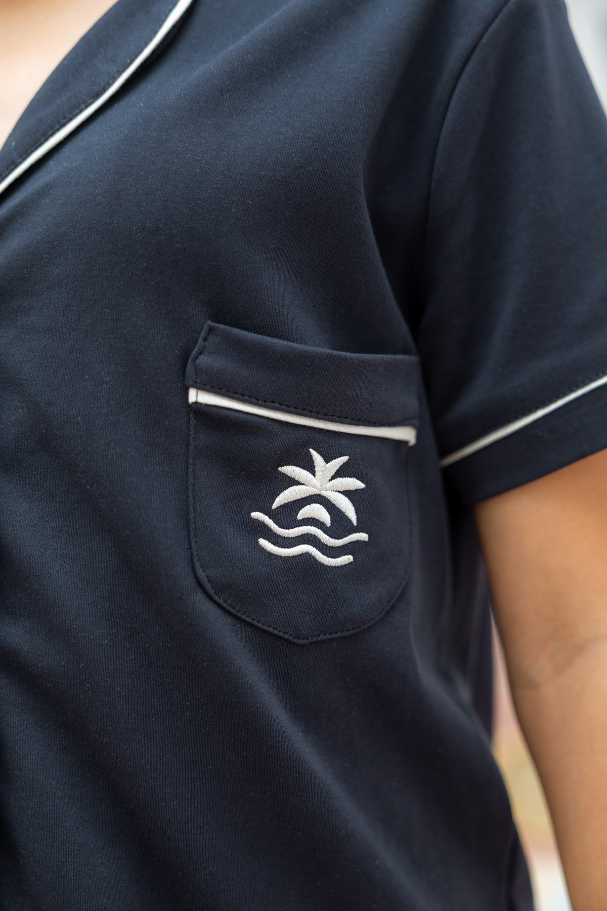 Close-up of the Neon94 Jellybean navy pyjama shirt chest pocket with embroidered palm-and-wave motif and white piping